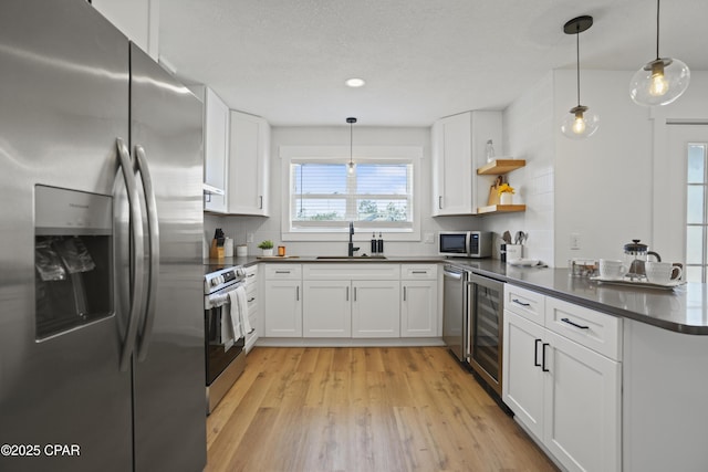 kitchen with light wood finished floors, stainless steel appliances, dark countertops, a sink, and a peninsula