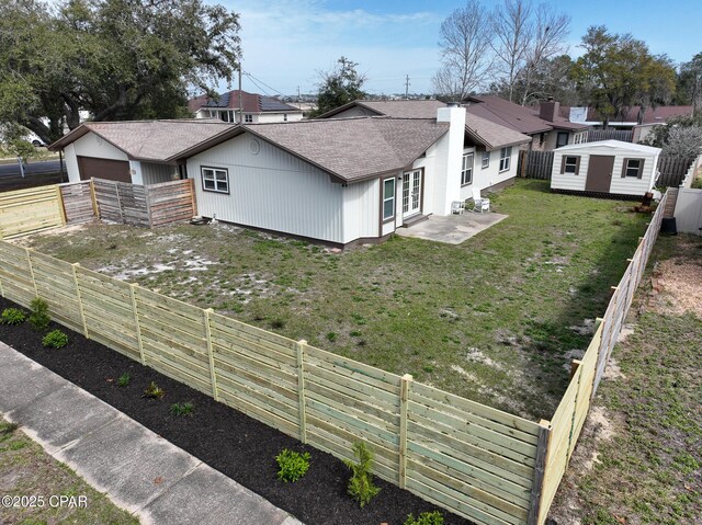 view of property exterior with a fenced backyard, an outdoor structure, roof with shingles, a lawn, and a chimney