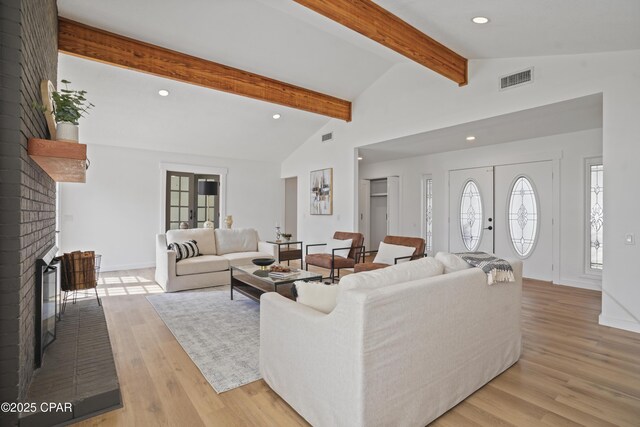 living area featuring lofted ceiling with beams, a fireplace, visible vents, french doors, and light wood finished floors