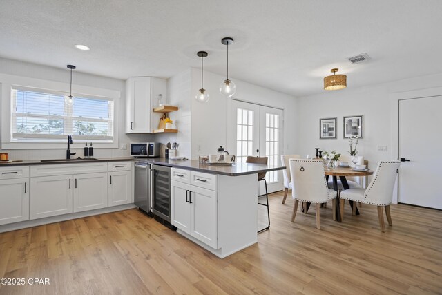 kitchen featuring a peninsula, a sink, visible vents, stainless steel microwave, and dark countertops