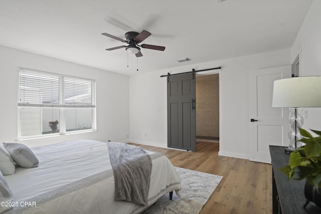 bedroom with a barn door, wood finished floors, visible vents, and baseboards