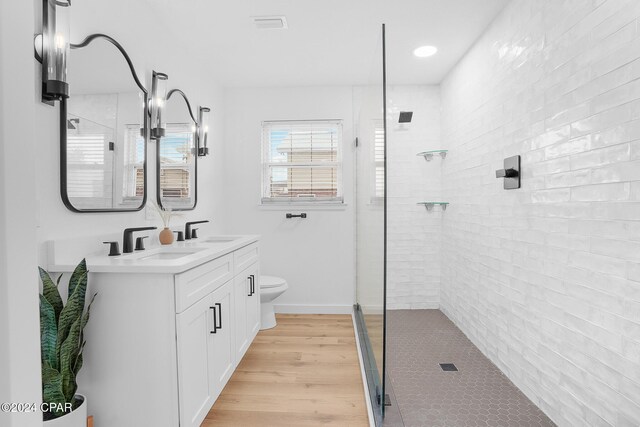 bathroom featuring a tile shower, wood finished floors, a sink, and toilet