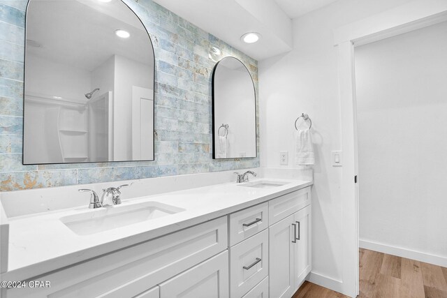 bathroom featuring double vanity, wood finished floors, walk in shower, and a sink