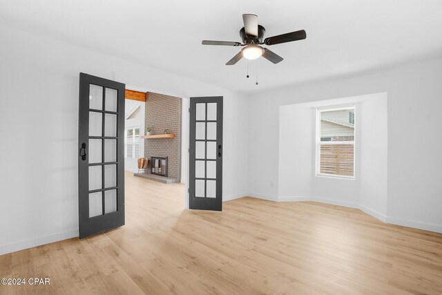 spare room with light wood-type flooring, french doors, baseboards, and a brick fireplace