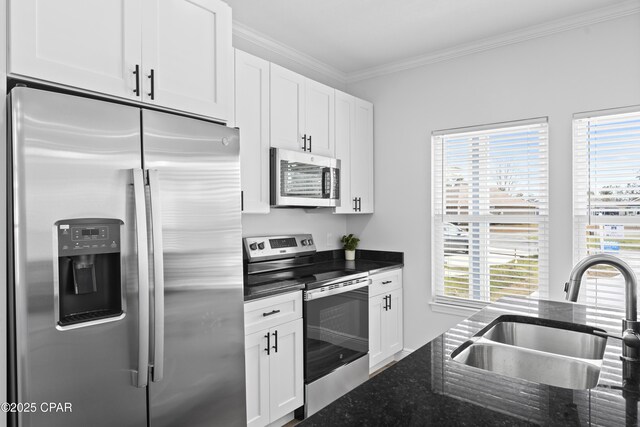 kitchen with sink, dark stone countertops, white cabinets, ornamental molding, and stainless steel appliances