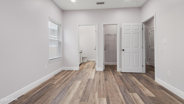 unfurnished bedroom with wood-type flooring, a walk in closet, ensuite bathroom, and a closet