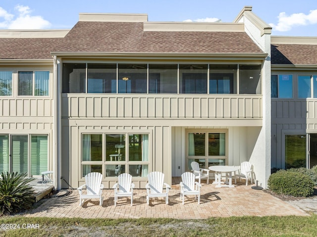 rear view of property with a sunroom, roof with shingles, board and batten siding, and a patio