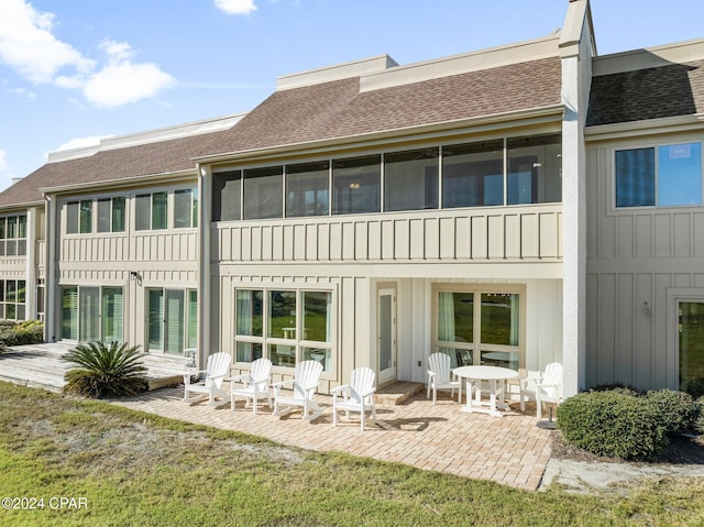 rear view of property with a sunroom, a shingled roof, board and batten siding, and a patio