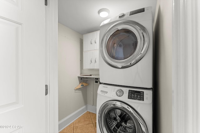 clothes washing area with stacked washer and dryer, cabinet space, baseboards, and light tile patterned floors