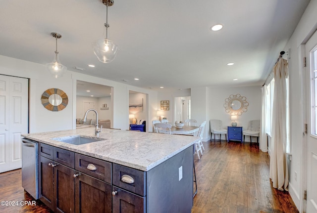 kitchen with stainless steel dishwasher, dark wood-type flooring, sink, decorative light fixtures, and a center island with sink