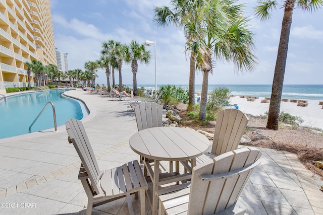 view of swimming pool with a water view, a beach view, and a patio