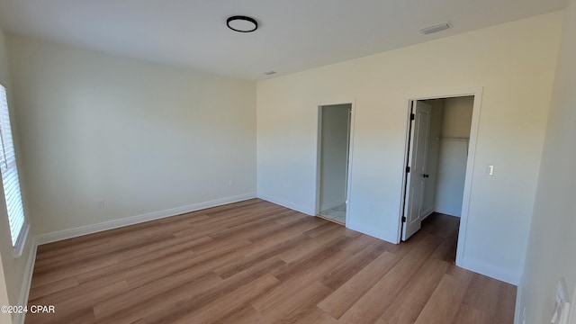 unfurnished bedroom featuring a spacious closet, a closet, and light wood-type flooring