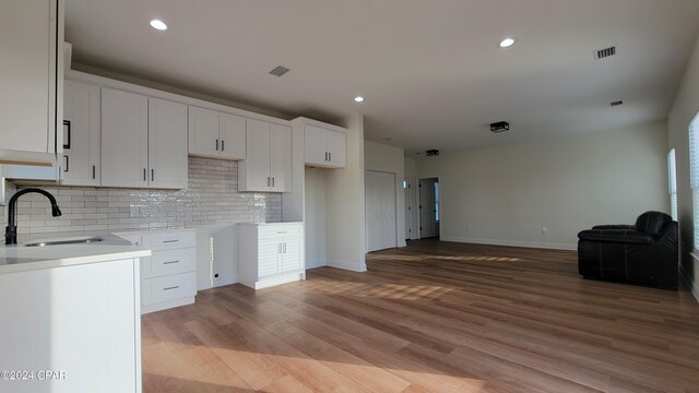 kitchen with tasteful backsplash, sink, light hardwood / wood-style flooring, and white cabinets