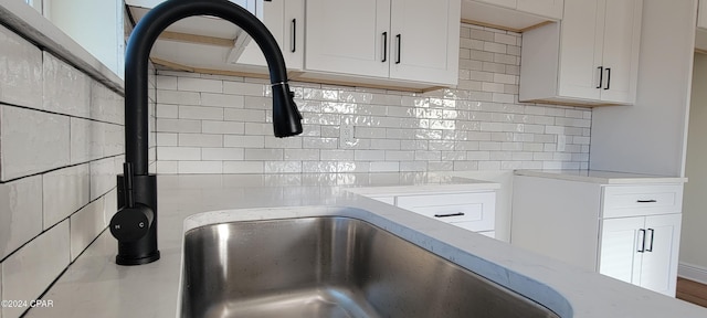 interior details featuring tasteful backsplash, light stone countertops, sink, and white cabinets