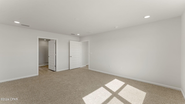 unfurnished bedroom with a spacious closet, a closet, and light colored carpet