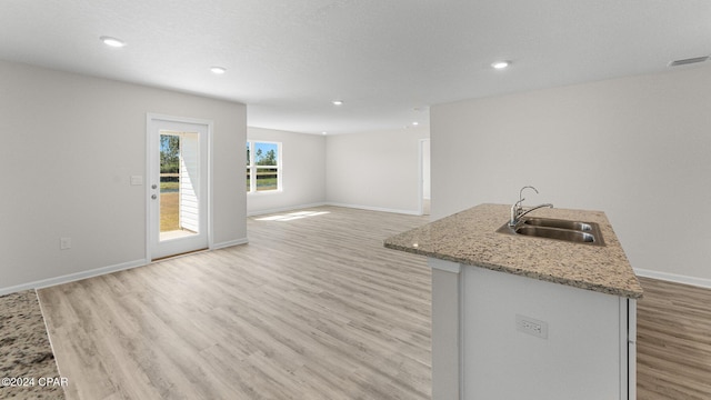 kitchen with light hardwood / wood-style floors, light stone counters, sink, and an island with sink