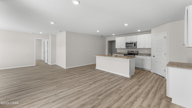 kitchen featuring light stone counters, appliances with stainless steel finishes, a center island with sink, white cabinets, and light wood-type flooring