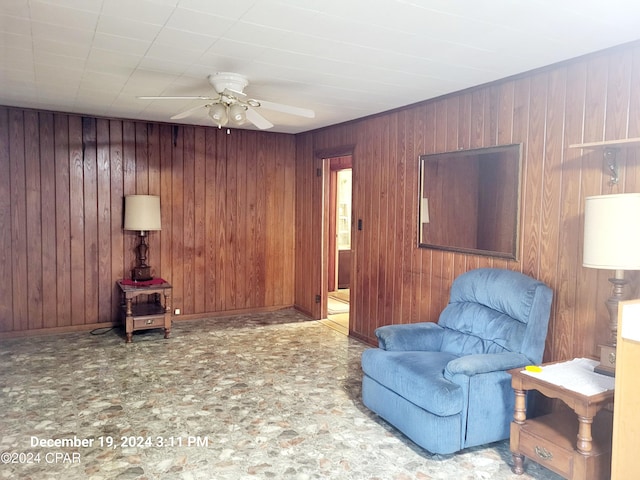 sitting room with ceiling fan and wood walls