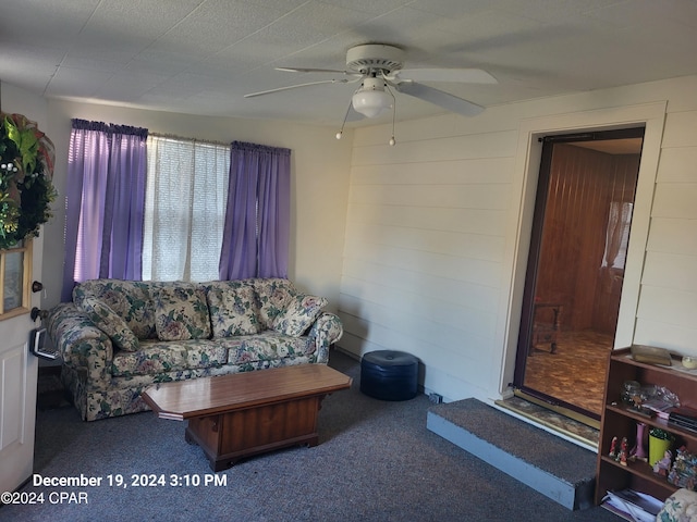 carpeted living room featuring ceiling fan and wooden walls