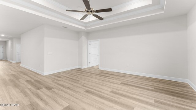 empty room featuring ornamental molding, a raised ceiling, and light wood-type flooring