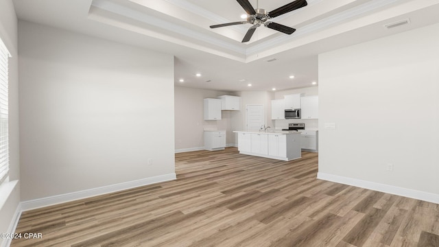 unfurnished living room featuring a tray ceiling, ceiling fan, light hardwood / wood-style floors, and ornamental molding