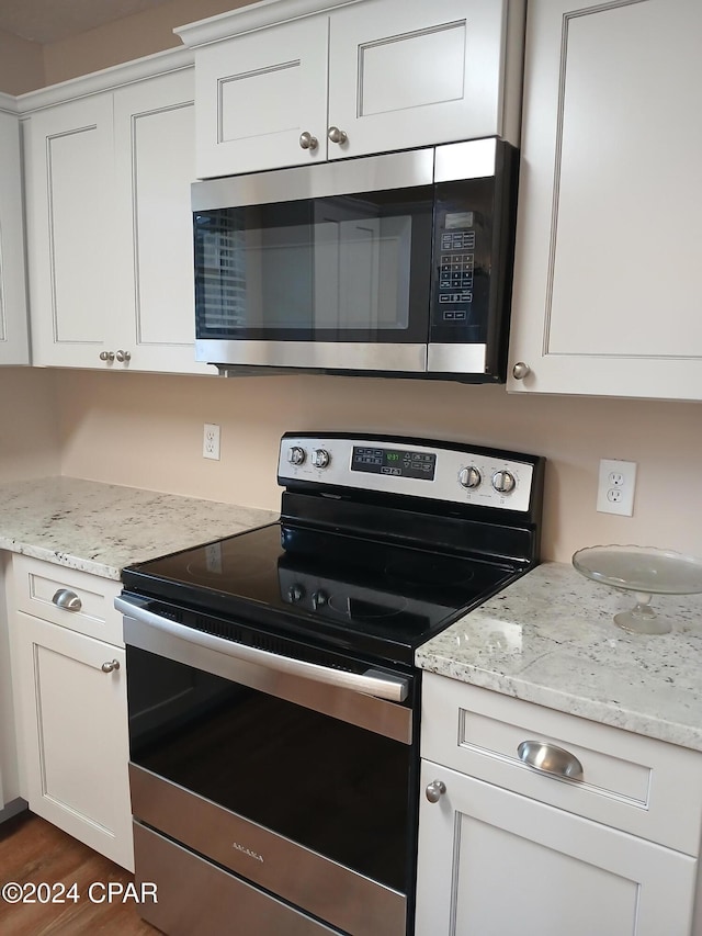 kitchen featuring dark hardwood / wood-style flooring, stainless steel appliances, white cabinetry, and light stone counters