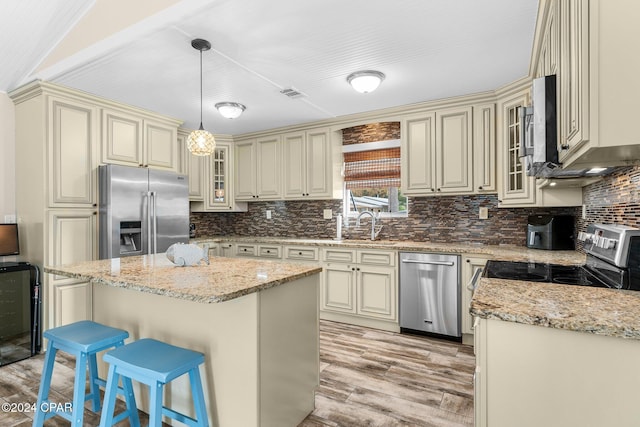 kitchen with a center island, light hardwood / wood-style flooring, pendant lighting, cream cabinetry, and appliances with stainless steel finishes