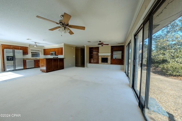 unfurnished living room with a tile fireplace, ceiling fan, light colored carpet, and ornamental molding