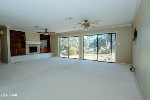 unfurnished living room with ceiling fan, built in features, crown molding, light colored carpet, and a tiled fireplace