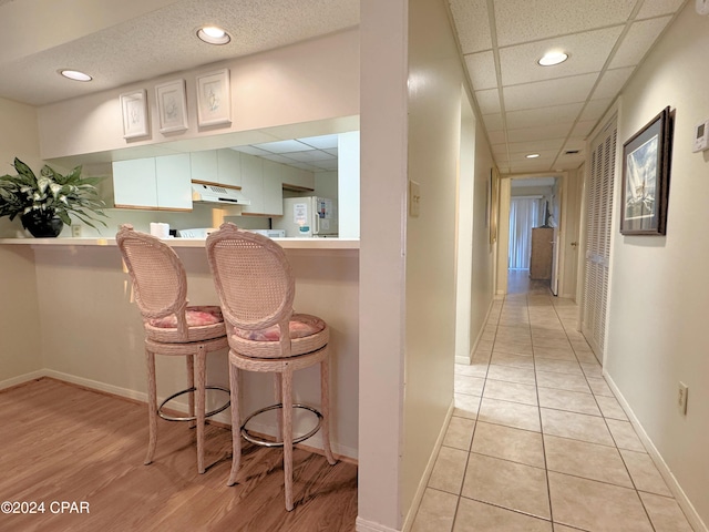 kitchen with kitchen peninsula, a paneled ceiling, refrigerator, a breakfast bar area, and light tile patterned flooring