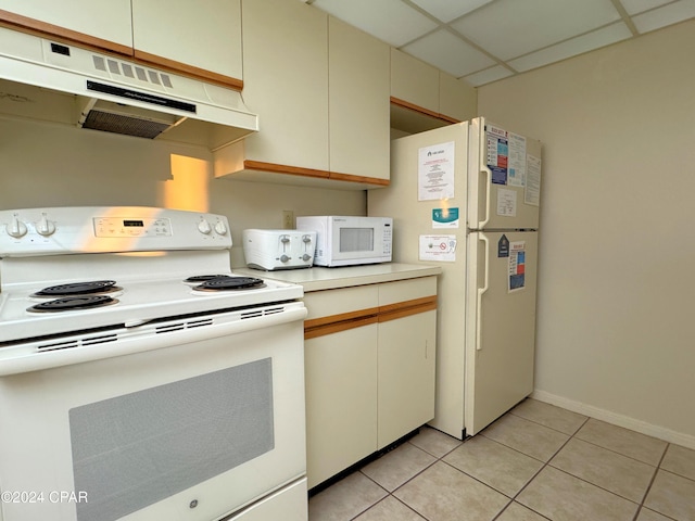 kitchen with cream cabinetry, white appliances, a paneled ceiling, and light tile patterned flooring