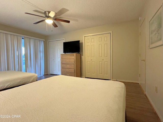 unfurnished bedroom featuring a textured ceiling, ceiling fan, wood-type flooring, and two closets