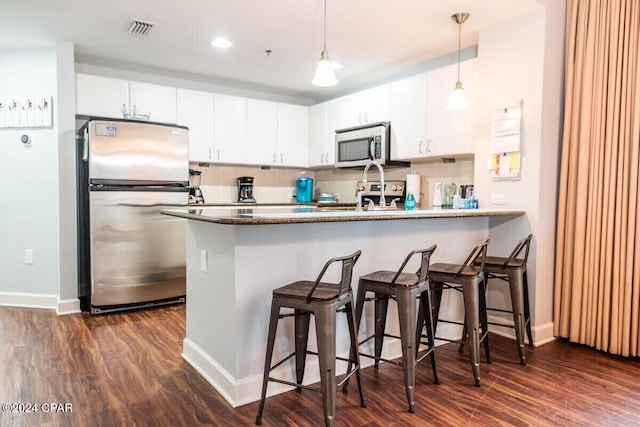 kitchen featuring dark hardwood / wood-style flooring, kitchen peninsula, pendant lighting, white cabinets, and appliances with stainless steel finishes