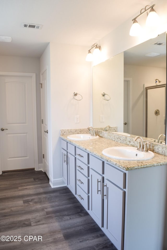 full bathroom with double vanity, visible vents, wood finished floors, and a sink