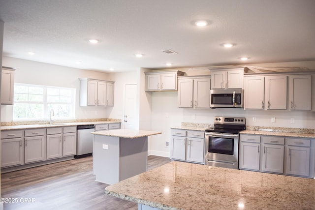 kitchen with visible vents, a sink, a kitchen island, wood finished floors, and appliances with stainless steel finishes