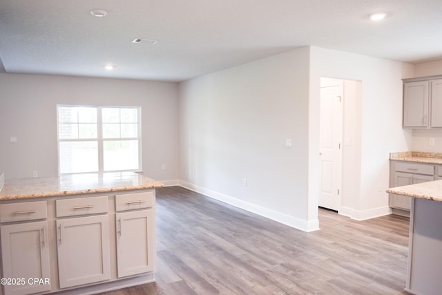 kitchen with gray cabinetry, visible vents, light wood-type flooring, and baseboards