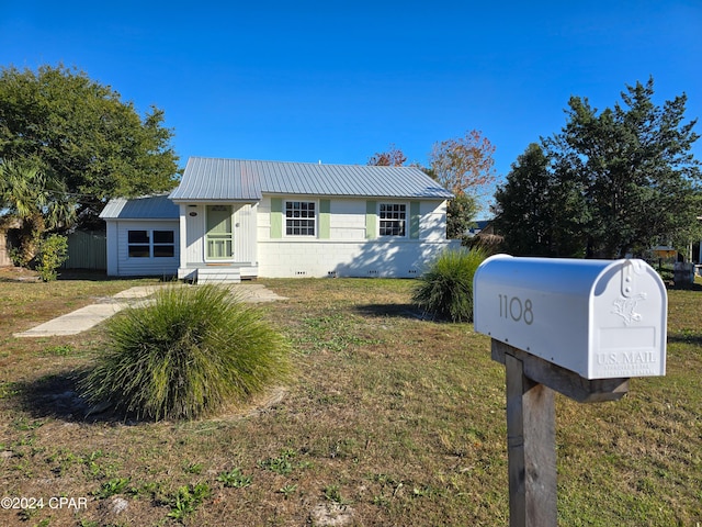 view of front of home featuring entry steps, concrete block siding, metal roof, and a front yard