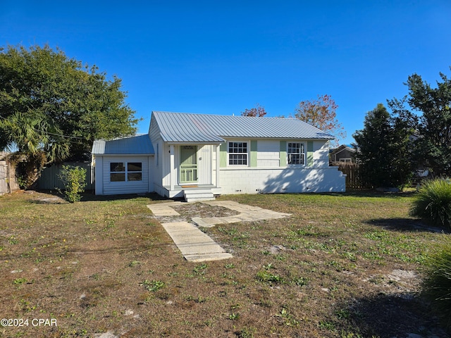 ranch-style home with concrete block siding, metal roof, a front lawn, and fence