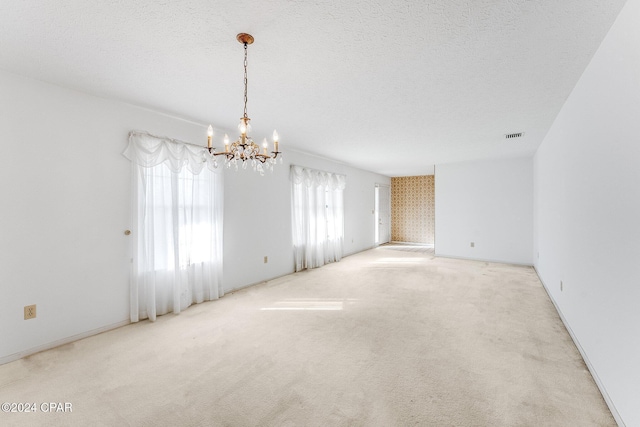 carpeted empty room featuring a textured ceiling and an inviting chandelier