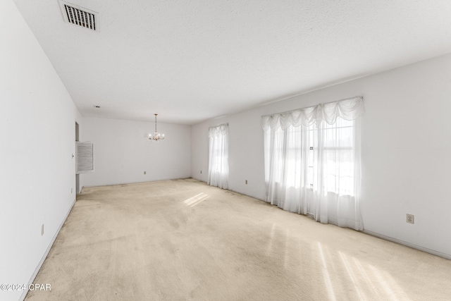 carpeted empty room featuring a notable chandelier, a healthy amount of sunlight, and a textured ceiling