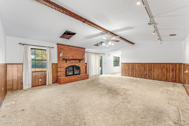 unfurnished living room featuring lofted ceiling with beams, a brick fireplace, ceiling fan, a textured ceiling, and light colored carpet