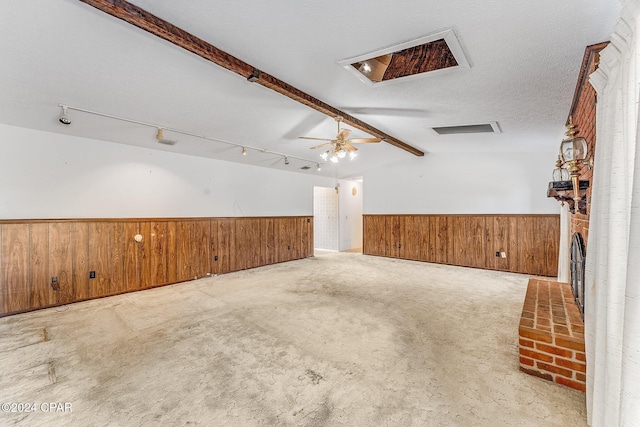 interior space with light carpet, rail lighting, a brick fireplace, a textured ceiling, and lofted ceiling with beams