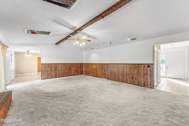 carpeted spare room featuring vaulted ceiling with beams, ceiling fan, rail lighting, and a textured ceiling