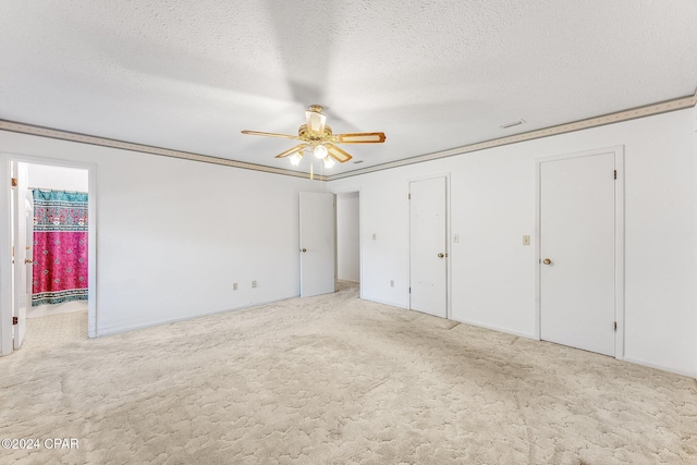 unfurnished bedroom with a textured ceiling, light colored carpet, ceiling fan, and crown molding