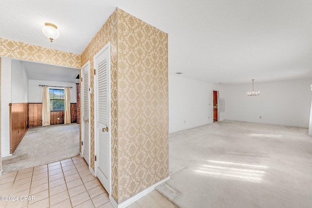 hallway featuring light colored carpet, wooden walls, and a chandelier