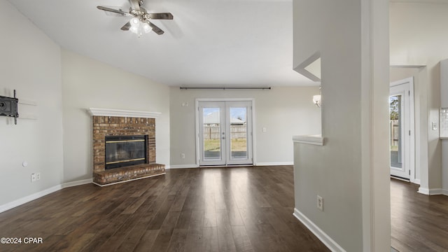 unfurnished living room featuring a wealth of natural light, ceiling fan, dark wood-type flooring, and a brick fireplace