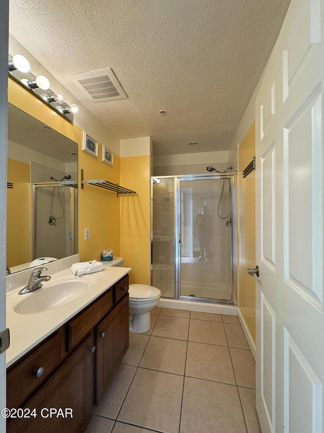 bathroom featuring tile patterned floors, a textured ceiling, toilet, a shower with door, and vanity