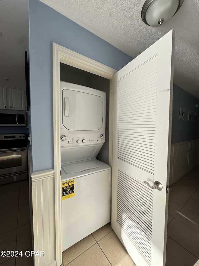 washroom with a textured ceiling, light tile patterned flooring, and stacked washer and dryer