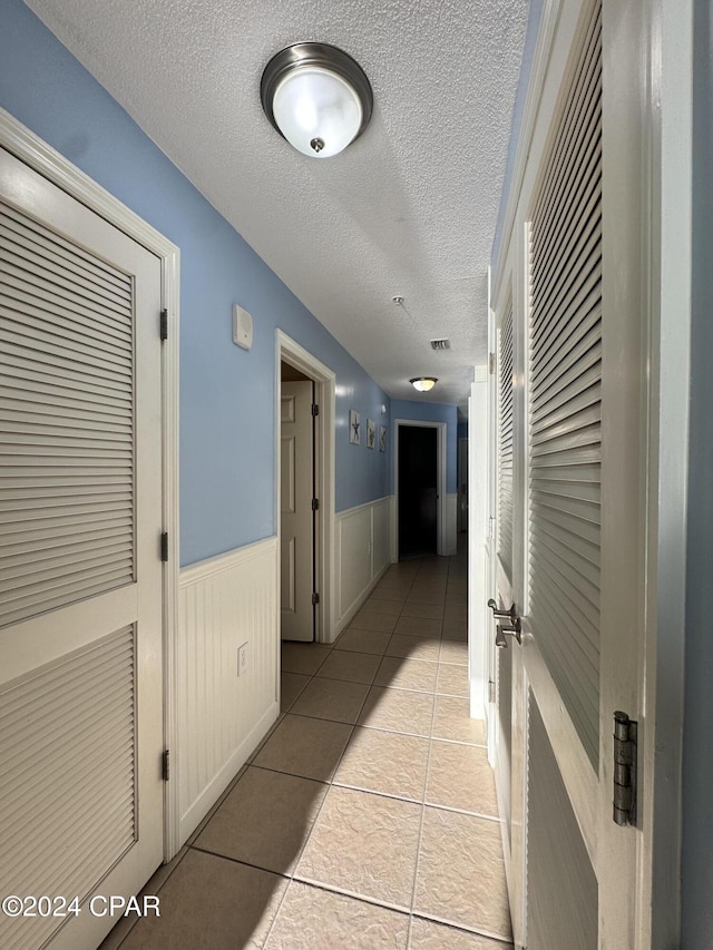 hall with light tile patterned flooring and a textured ceiling