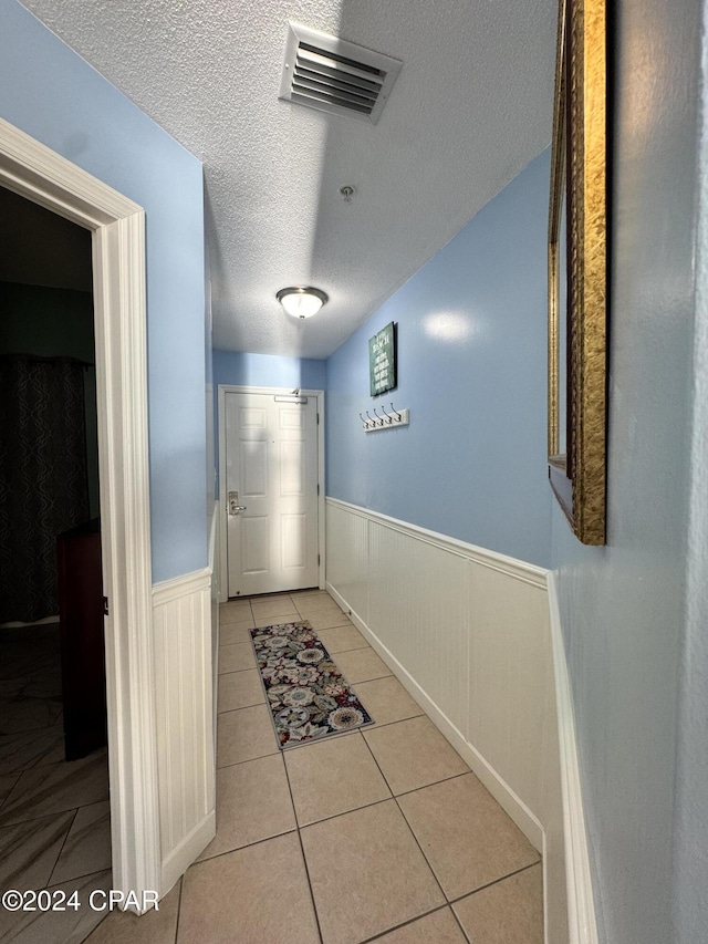 hall featuring wood walls, light tile patterned flooring, and a textured ceiling